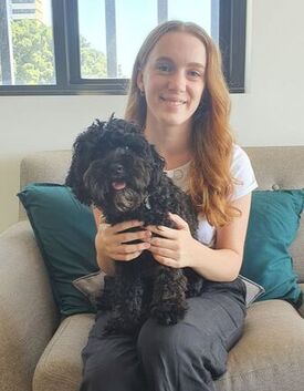 Speech Pathologist sitting on a couch smiling with a black dog on their lap